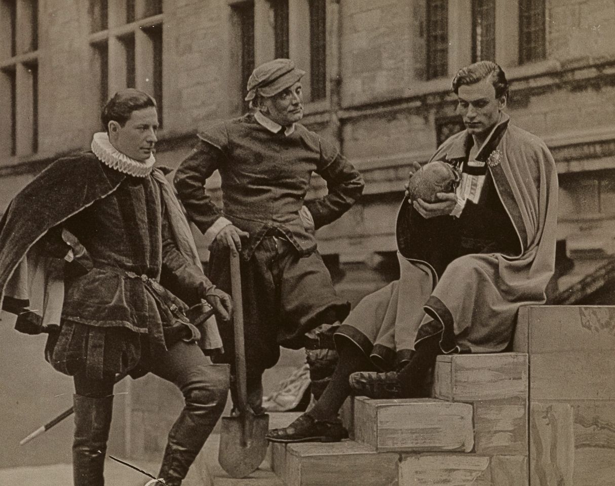 Historisk arkivfoto af tre skuespillere i renæssancekostumer på trapper foran Kronborgs facade – tidlig Hamlet-opførelse på slottet