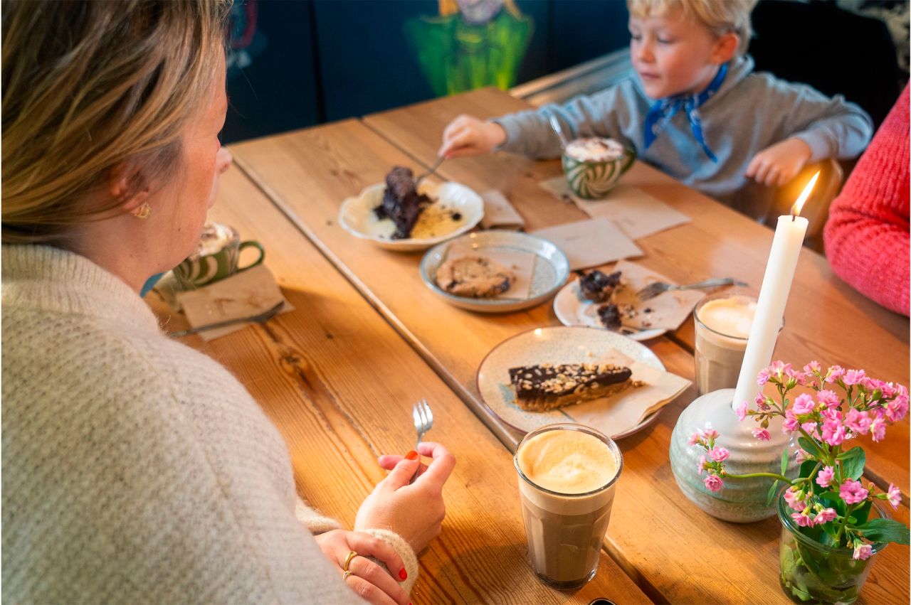 Familie spiser kage og drikker kaffe i Kronborgs café – hyggelig stemning med levende lys og friske blomster